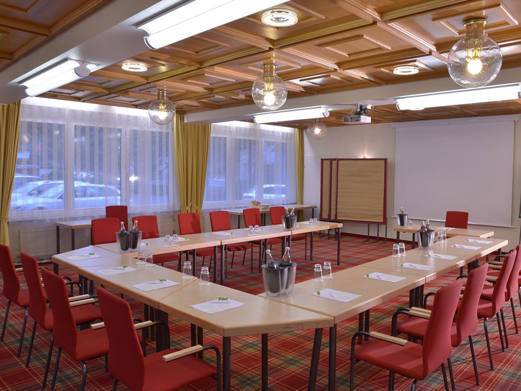 A conference room with long tables, red chairs, and a projector screen.