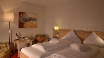A hotel room with a bed, a desk with a lamp, a chair, and a painting on the wall.
