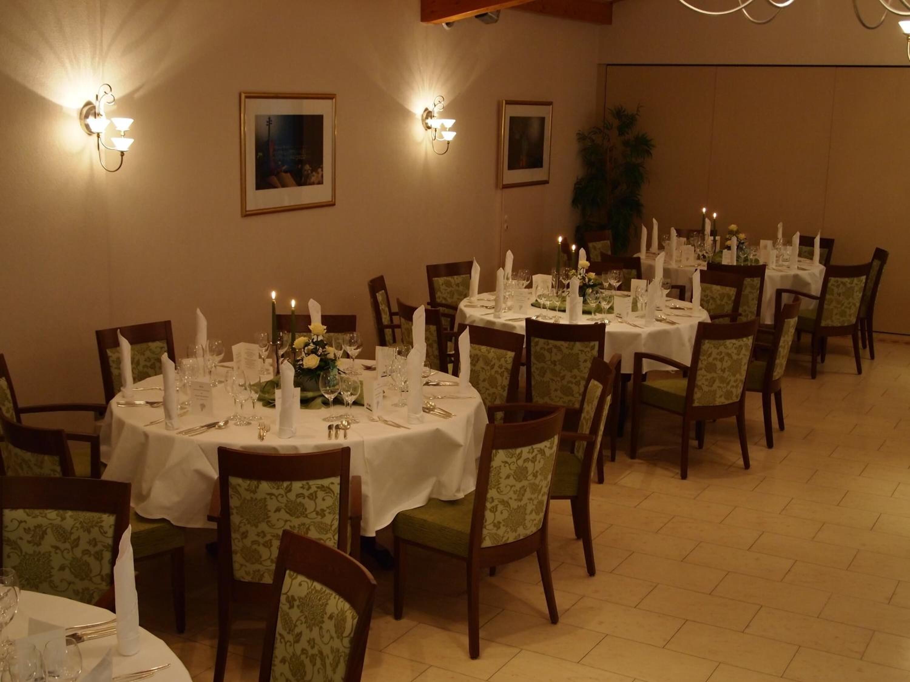 A dining area with round tables set for four, each with a white tablecloth, candles, and floral centerpieces.