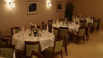 A dining area with round tables set for four, each with a white tablecloth, candles, and floral centerpieces.