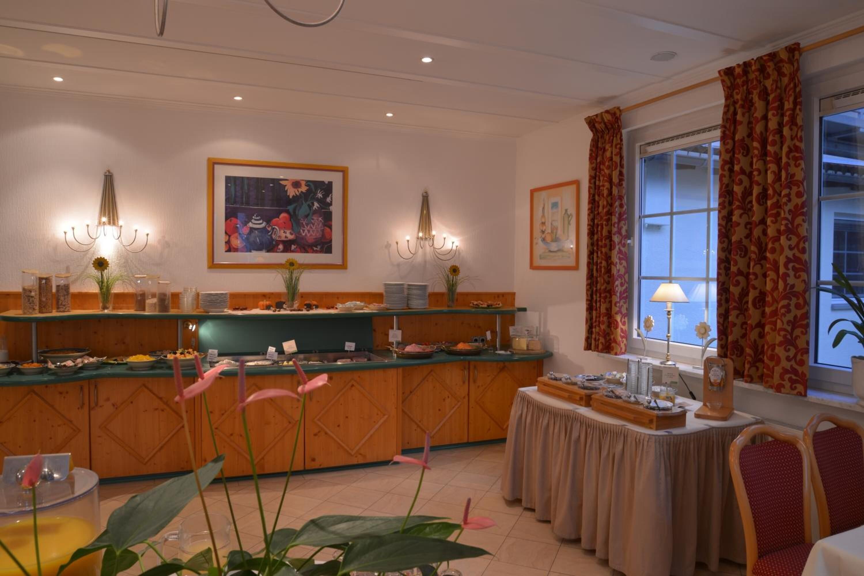 A hotel room with a breakfast bar, a dining table, and a window with curtains.