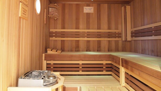 A sauna with wooden walls and benches, a heater, and a sign indicating the temperature. - Parkhotel zum Stern (Oberaula)