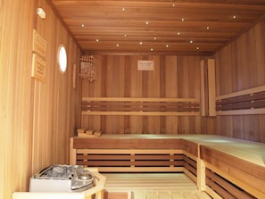 A sauna with wooden walls and benches, a heater, and a sign indicating the temperature. - Parkhotel zum Stern (Oberaula)