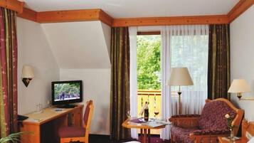 A hotel room with a bed, a desk with a television, a chair, a small table with a wine glass, and curtains.