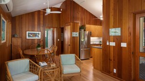 A wooden-paneled room with a dining table, chairs, a refrigerator, and a ceiling fan. - Waialea Bay Beachfront Home with AC (Kamuela)