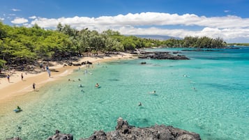A beach with clear turquoise water, rocky shoreline, and lush greenery.