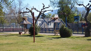 A fenced park area with a playground, benches, and a thatched-roof shelter. - mobile home 2018 with terrace (Argelès-sur-Mer)