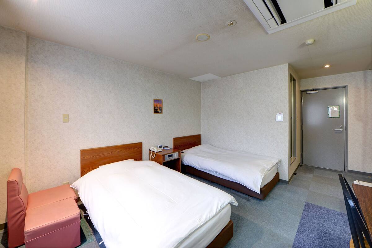 A hotel room with two single beds, a wooden headboard, a small desk with a telephone, and a door to the bathroom.