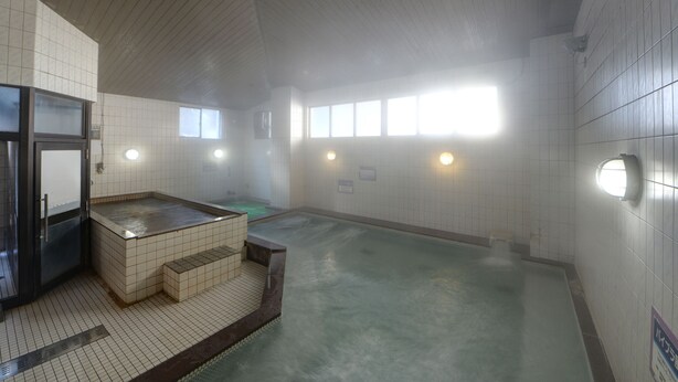 Una amplia piscina cubierta con zona de sauna, paredes de azulejos y techo de madera.