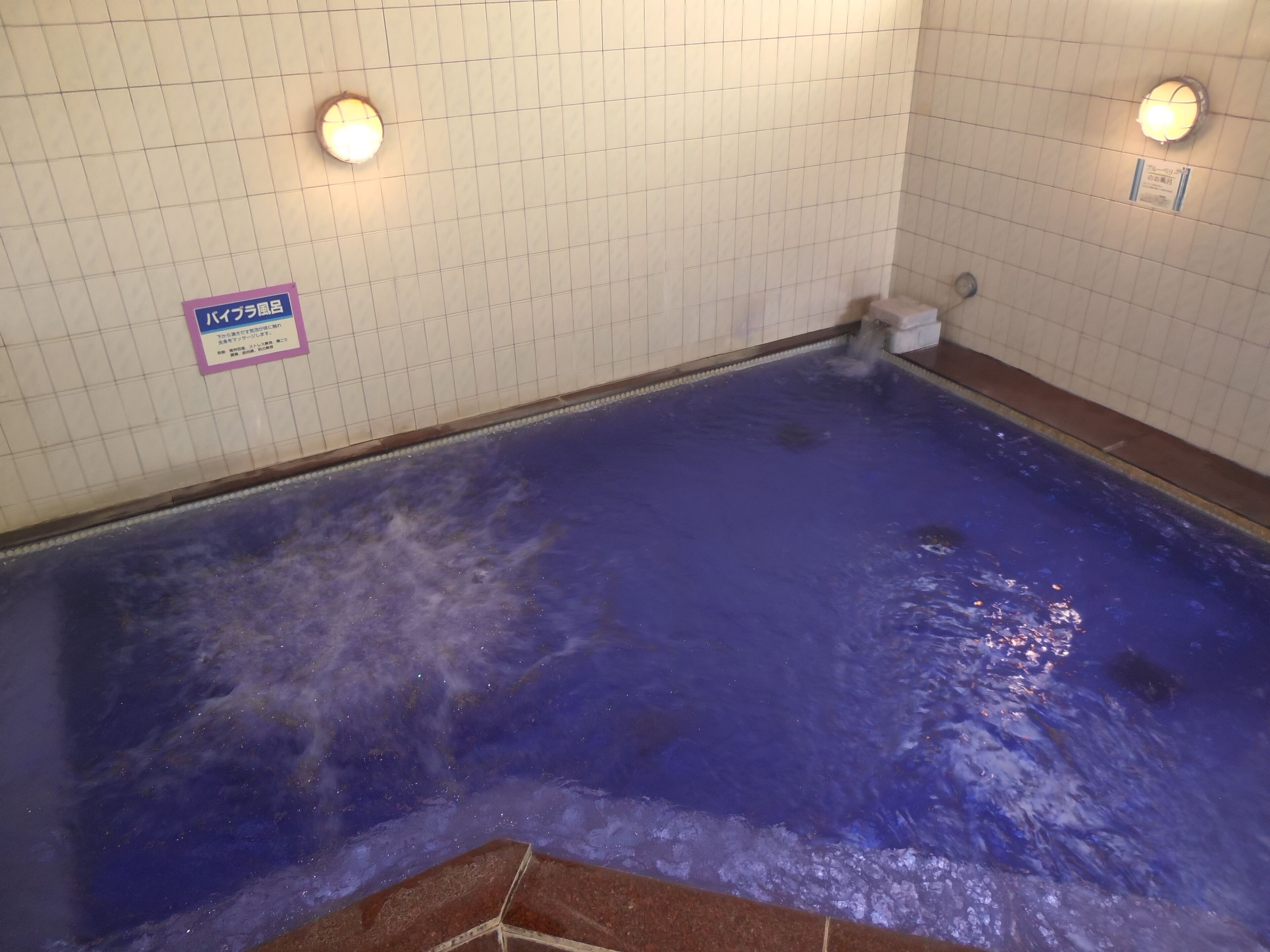 A swimming pool with a blue water feature, tiled walls, and two wall-mounted lights.