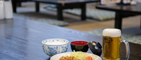 A dining table with a plate of food, a bowl of rice, a small bowl of sauce, and a mug of beer.
