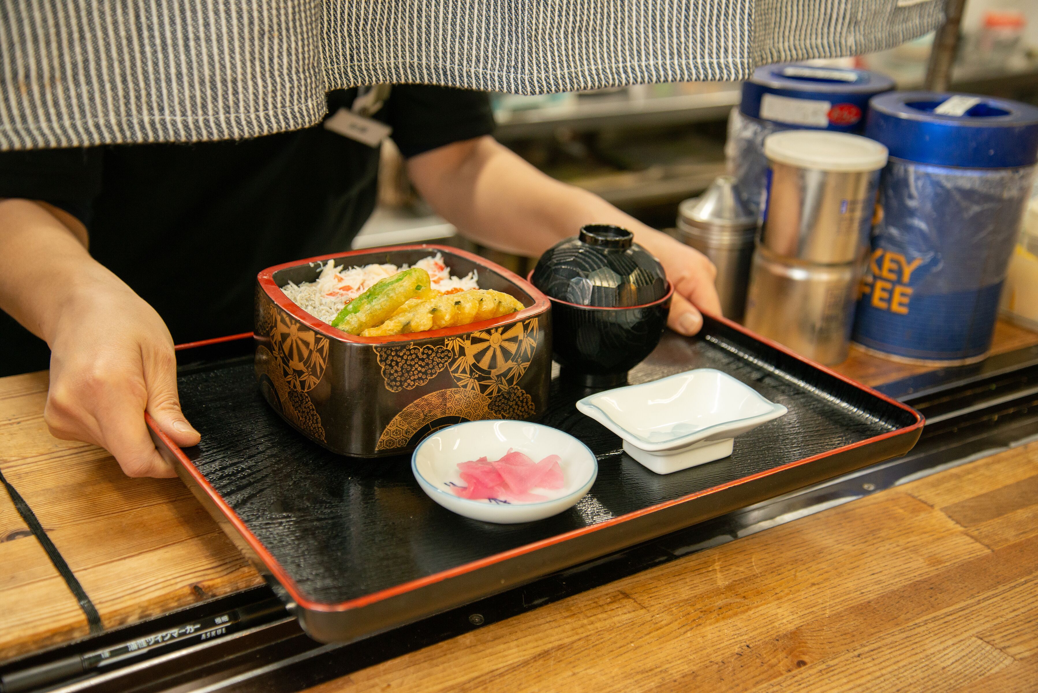 A tray with food items, including a bowl of rice, vegetables, and a small dish of pink pickled ginger.