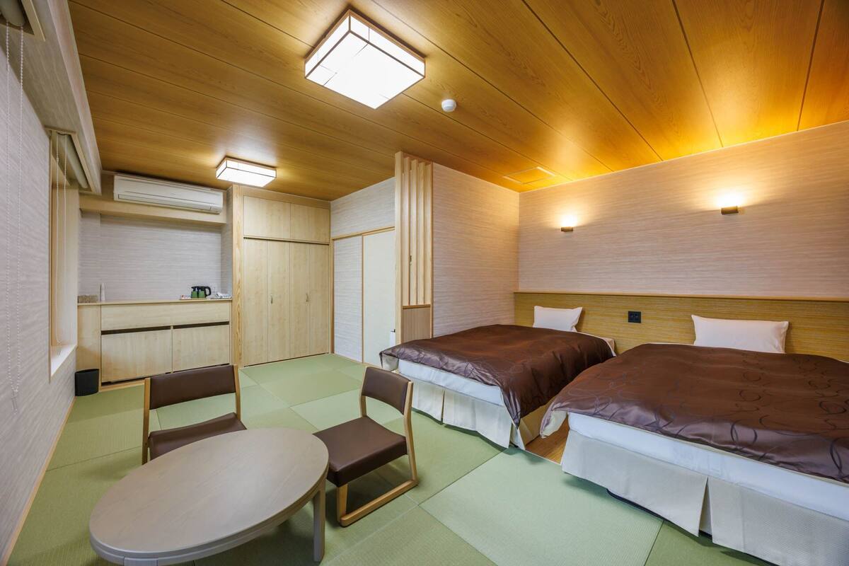Kompakti hotellihuone, jossa on kaksi sänkyä, pieni pöytä, tuolit, minikeittiö ja kattoikkunoilla varustettu katto.