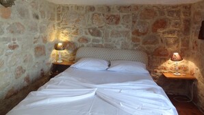 A room with a bed, two bedside tables, and a stone wall. - rosalia apartment    (Chalki)