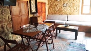 A cozy dining area with a wooden table and chairs, a sofa, and a stone wall. - rosalia apartment    (Chalki)