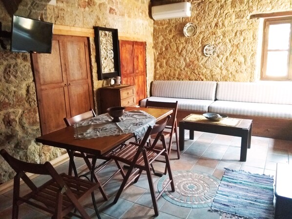 A cozy dining area with a wooden table and chairs, a sofa, and a stone wall.