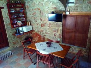 A dining area with a stone wall, a television mounted above a wooden cabinet, and a table with chairs.