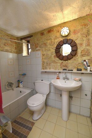 A bathroom with a toilet, sink, and bathtub. There is a mirror on the wall and toiletries on the sink.