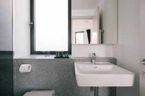 Een moderne badkamer met een witte wastafel, een granieten aanrechtblad en een raam boven de wastafel.