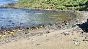 A beach with a rocky shoreline, a small body of water, and a hill with sparse vegetation and a few buildings. - TOI ET MOI -  our reviews speek for us ! (Ponta Delgada)
