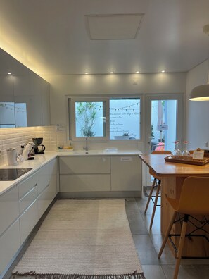 A modern kitchen with white cabinetry, a built-in oven, a coffee machine, and a window with plants.