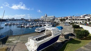 A marina with boats docked, a large building in the background, and a clear blue sky. - TOI ET MOI -  our reviews speek for us ! (Ponta Delgada)