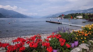 Une vue sur le lac, avec une jetée qui s’avance dans l’eau, entourée de fleurs aux couleurs vives et, au loin, des montagnes.