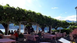 Un café en plein air avec des tables recouvertes de nappes roses, entouré de verdure et donnant sur une étendue d’eau.