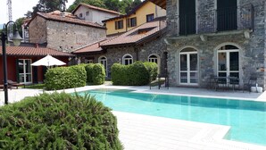 Une piscine entourée de bâtiments en pierre dotés d’arcs et de fenêtres en ogive, ainsi qu’un patio aménagé avec du mobilier d’extérieur.
