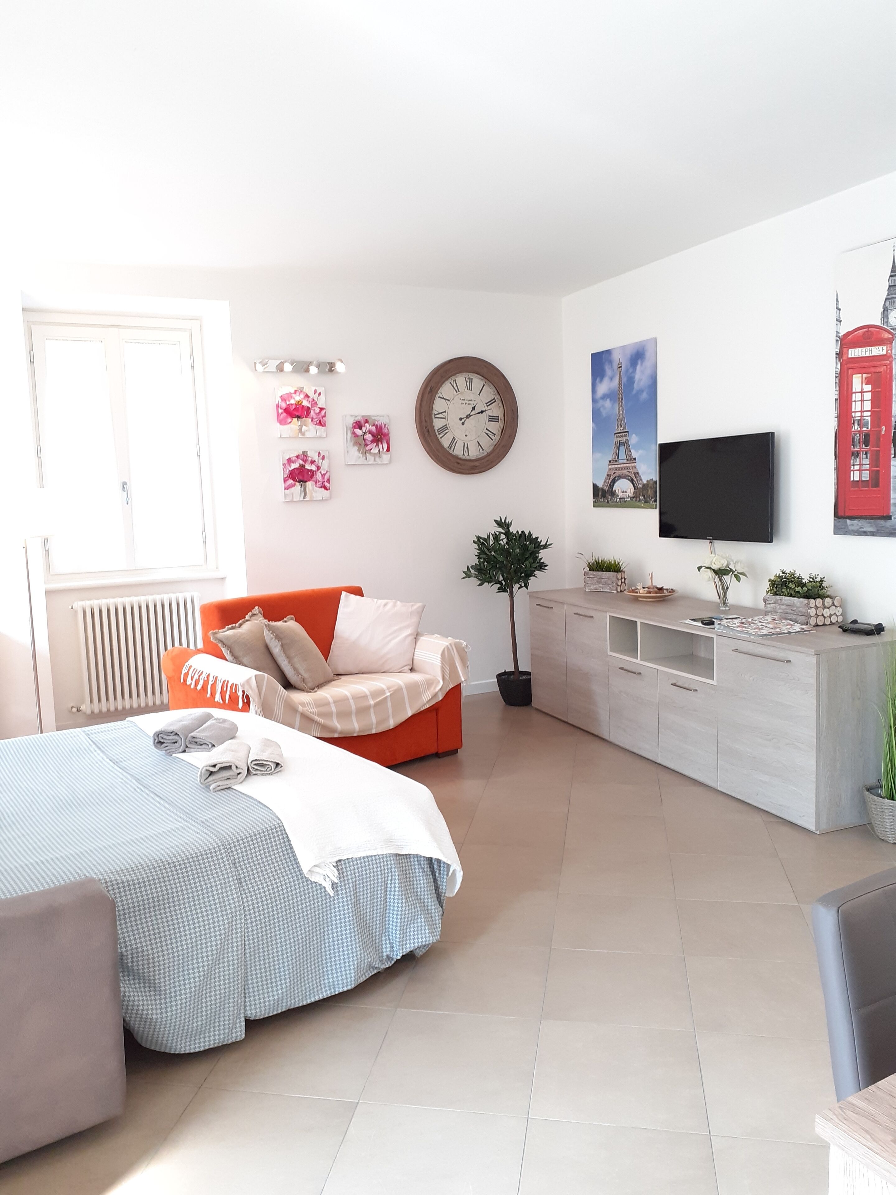 Een moderne slaapkamer met een bed, een bank, een televisie en een klok aan de muur.