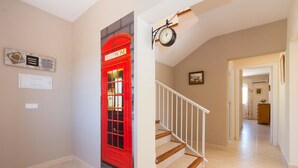 Un couloir avec une cabine téléphonique rouge, une horloge et un escalier.