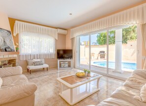 A spacious living room with a fireplace, comfortable seating, a television, and a view of a swimming pool. - Villa DELICIA by Abahana Villas (Calpe)