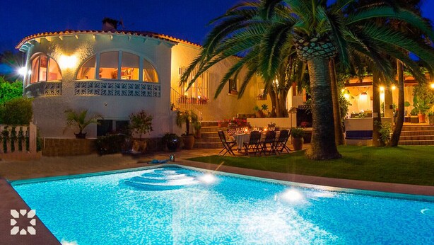 A poolside view of a building with a pool, palm trees, and outdoor seating.