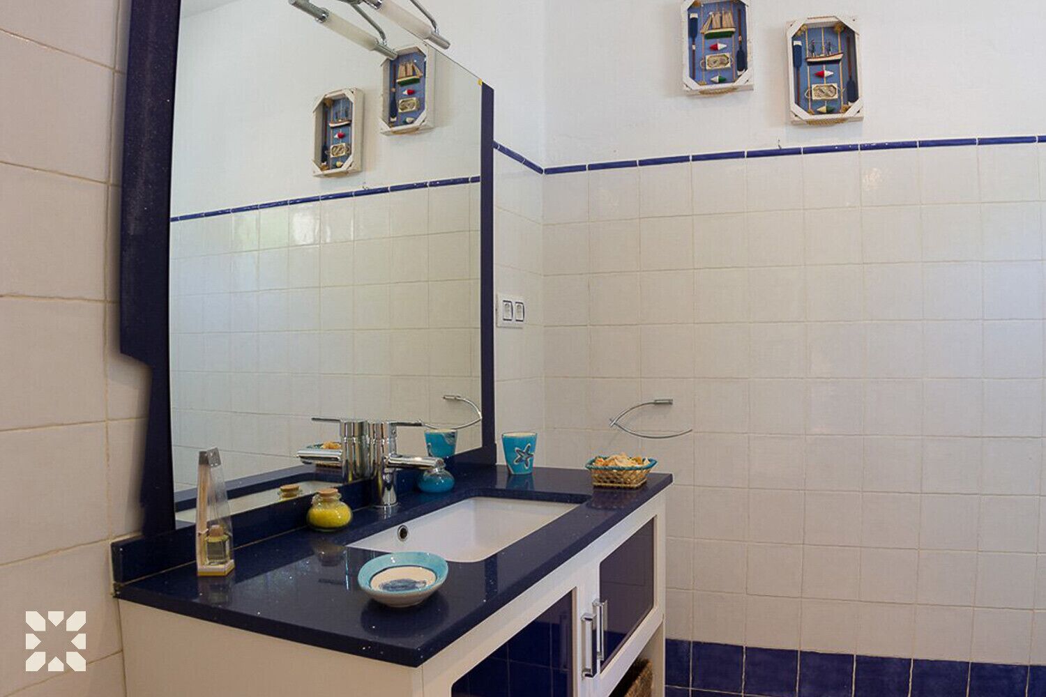 Een badkamer met een grote spiegel, een wastafel met een blauw aanrechtblad en een witte betegelde muur.