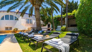 A poolside area with sun loungers, towels, and a palm tree.