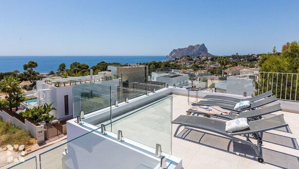 Una terraza en la azotea con piscina de vidrio, sillones de descanso y vistas al mar y a la montaña.