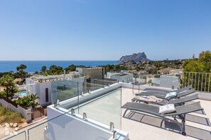 Eine Dachterrasse mit Glaspool, Liegestühlen und Blick auf Meer und Berge.