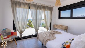 Un dormitorio con una cama grande, vistas al mar y una silla con un cojín colorido.