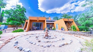 A house with a circular rock garden, a patio with chairs, and a small fountain.