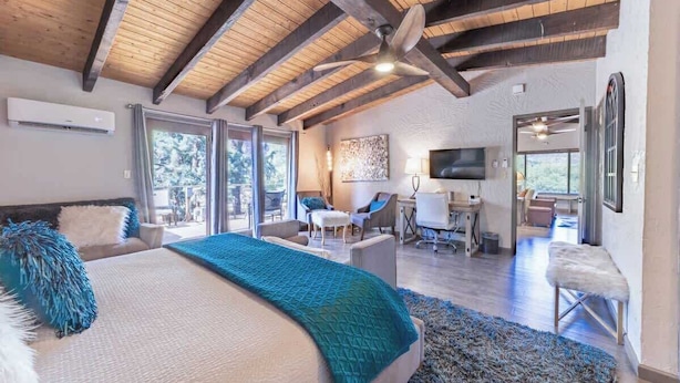 A bedroom with a large bed, a desk, and a chair, a balcony with a view, and a ceiling fan.