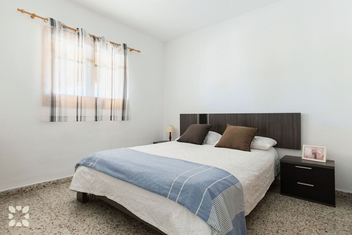 A bedroom with a bed, nightstand, and a picture frame on the nightstand.