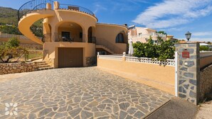Un edificio de estilo mediterráneo con un balcón curvo, entrada de adoquines y una pared de piedra con un buzón de seguridad.