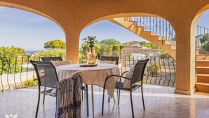 Un espacio al aire libre cubierto con una mesa redonda y sillas, un jarrón decorativo, y vistas a una escalera y follaje.