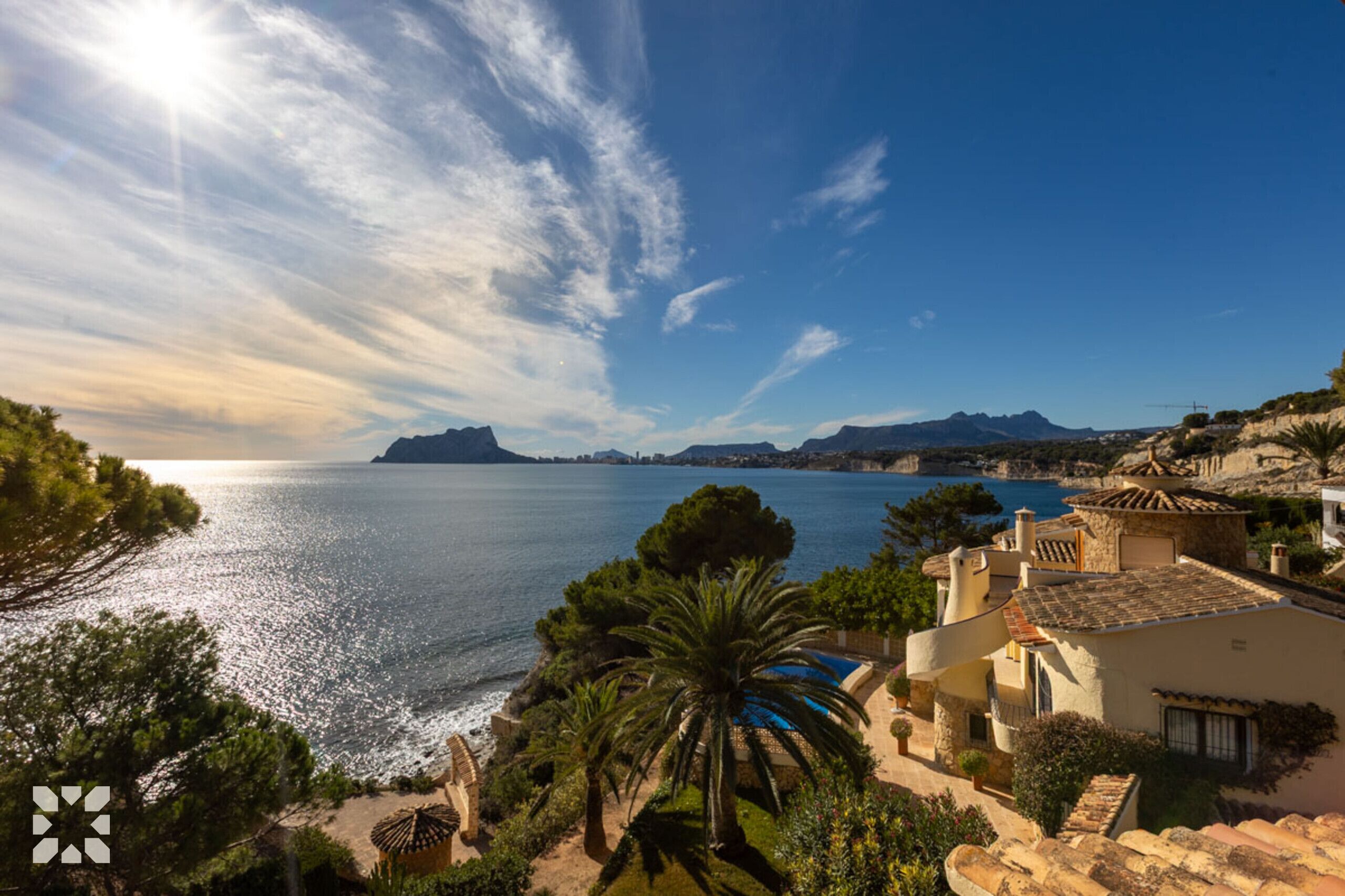 A coastal view with a clear sky, a calm sea, and a mountainous backdrop.