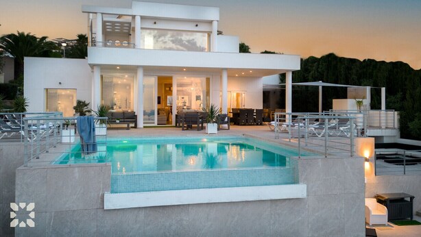 Una casa moderna de dos pisos con piscina, mobiliario exterior y un interior bien iluminado.