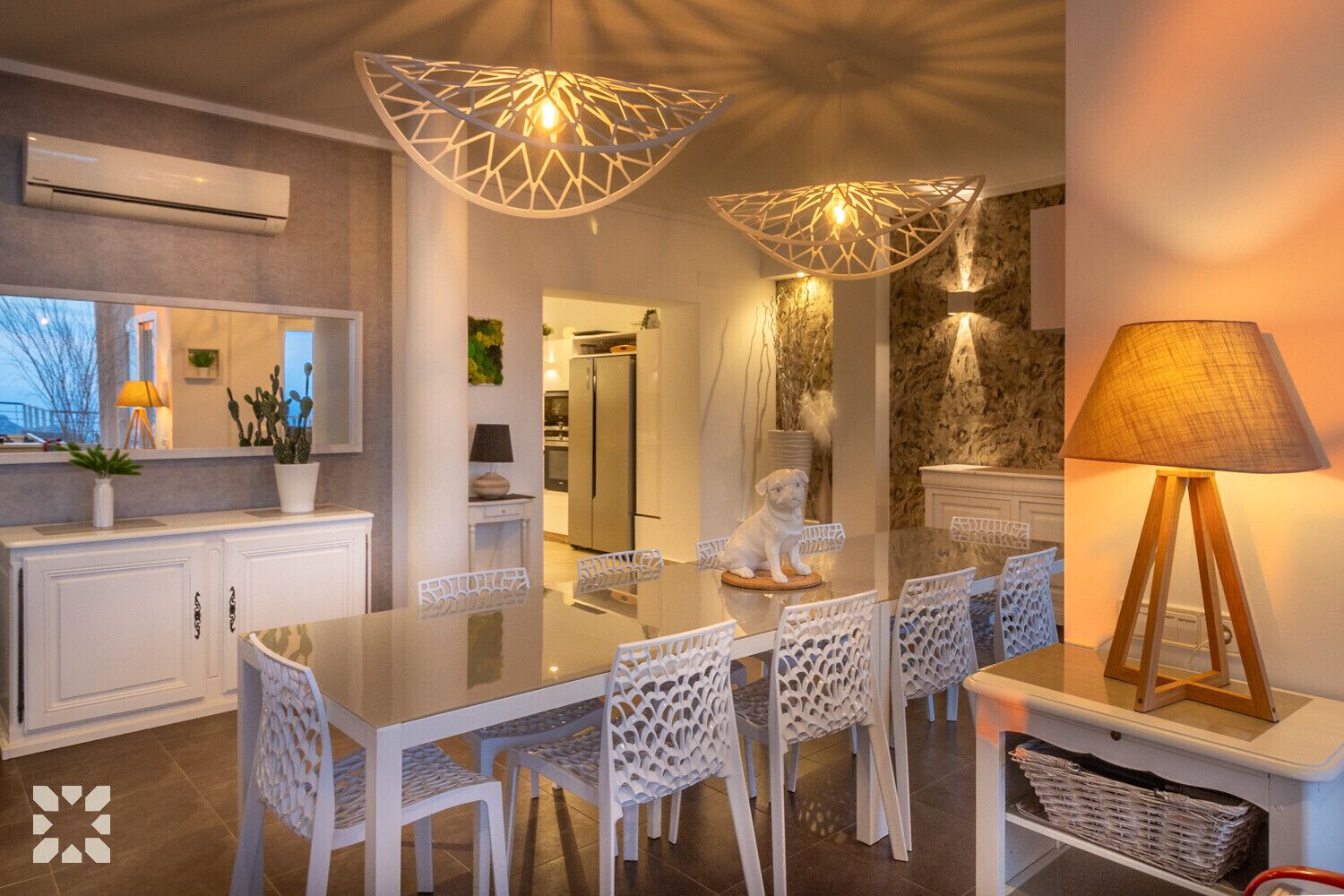A modern kitchen with white cabinetry, a central island, and a dining area with white chairs and a glass table.