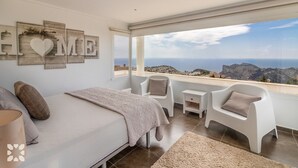 Un dormitorio con cama, mesita de noche, silla y vista al mar.