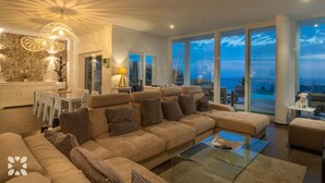 Un salón amplio con un sofá grande, una mesa de centro de vidrio y vistas al mar a través de amplios ventanales.