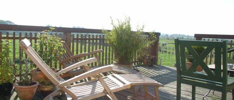 Una terraza de madera con dos sillones de descanso y una mesa, rodeada de plantas en macetas.