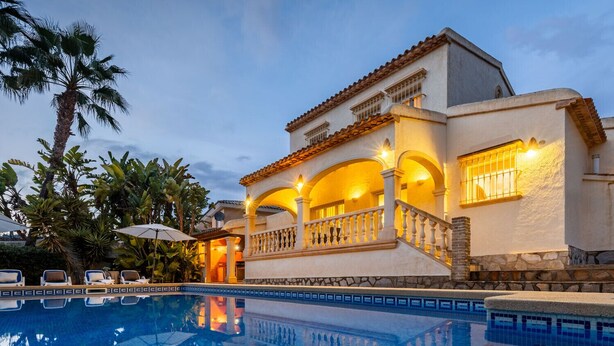 A luxurious villa with a swimming pool, featuring a Mediterranean architectural style with arches and a tiled roof.